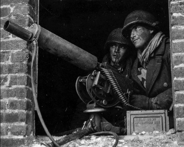 Soldier manning a .30 machine gun, with K-ration boxes stuffed into the front of his overcoat.