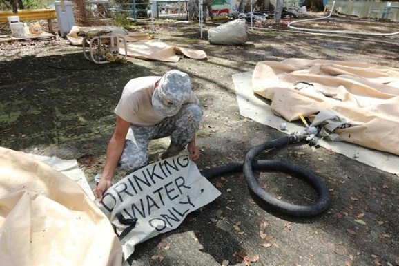 Soldier labeling water bladder with “Drinking Water Only” sign.