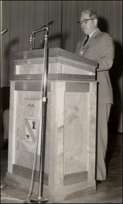 General McNamara standing behind a podium, dedicating the new building, “Mifflin Hall”, to the memory of Tom Mifflin.