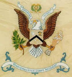 An Eagle looking right with wings open. It's Holding an olive branch in the right claw and arrows in the left; above a decorative banner with “Quartermaster Corps Regiment”