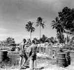 Two Soliders stand next to several 55 gallon drums in a POL storage area.